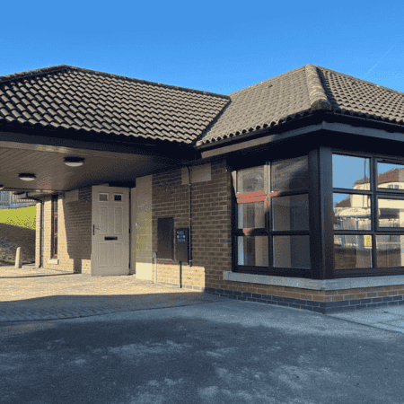 outside of the assisted living care home. the building has brown tiles and brown brick. it is a clear sunny day with blue skies